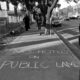 "no hotels on public land" written in sidewalk chalk black and white photograph